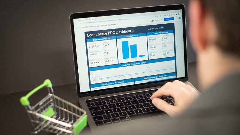Laptop showing an ecommerce PPC analytics dashboard with a small shopping trolley beside it