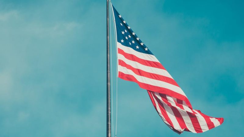 American flag flying from a tall flagpole against a blue sky with soft clouds