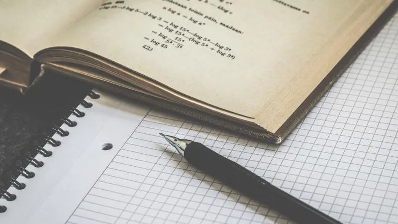 Open maths book with formulas, graph paper and a pen